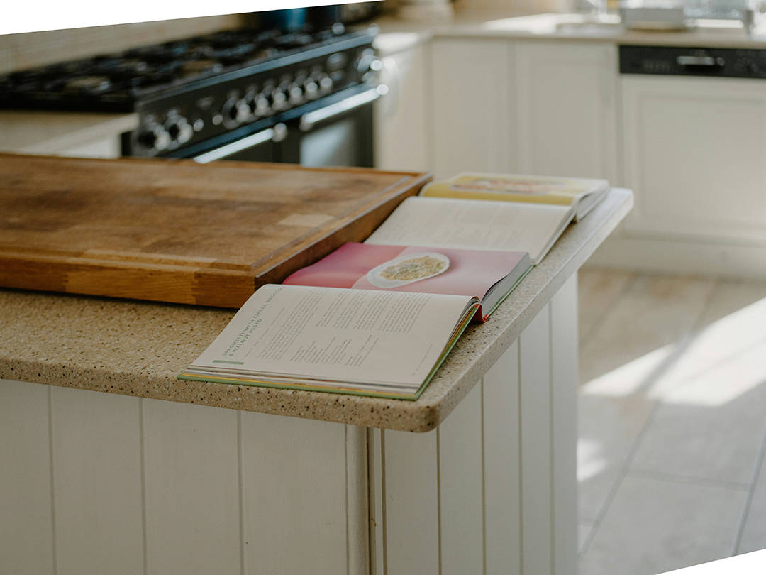 Open recipe books rest on a beige kitchen counter, next to a wooden cutting board.