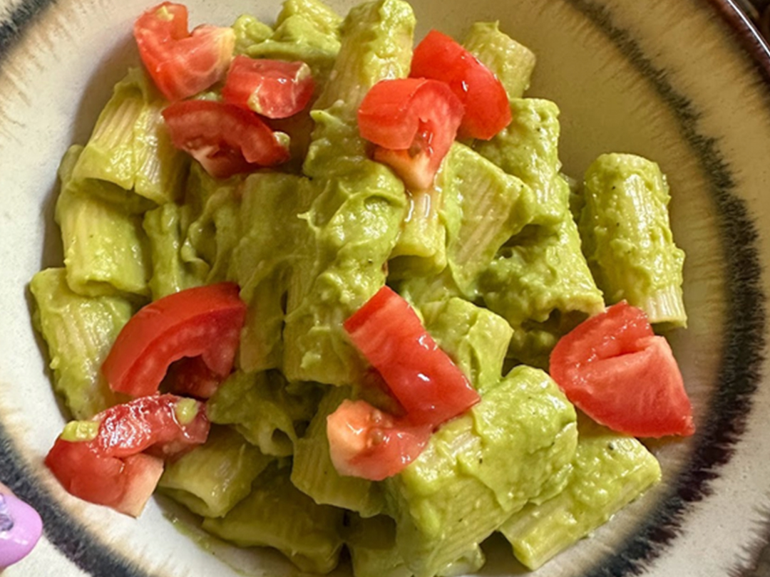 Bowl of pasta with an avocado sauce and cut tomatoes.