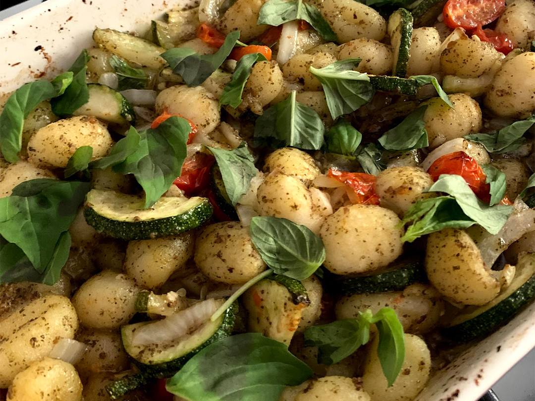 Close up of a gnocchi dish in a pan, with fresh tomatoes and herbs, in an oil based sauce.