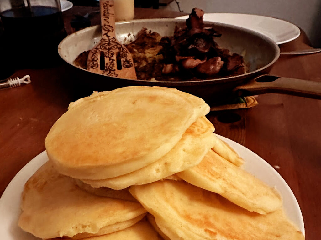Stack of fluffy buttermilk pancakes with. a skillet and spatula in the background of condiments.